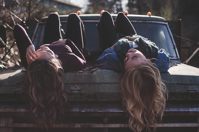 Dve dievčatá s dlhými vlasmi ležia na kapote starého auta